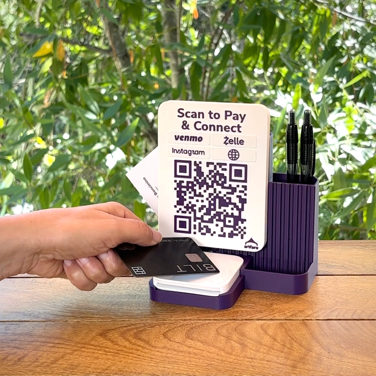 Customer tapping a card on a Square Reader in a purple Shopkeeper dock with Scan to Pay and Connect QR sign