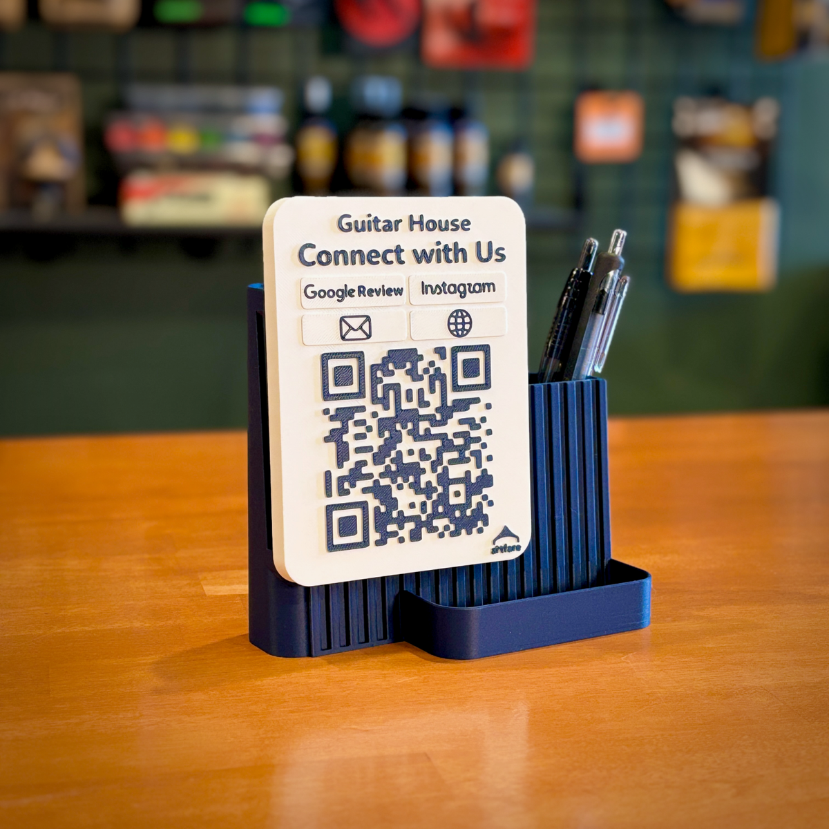 Navy Shopkeeper Guitar House social media QR sign with pens on a wooden shop counter